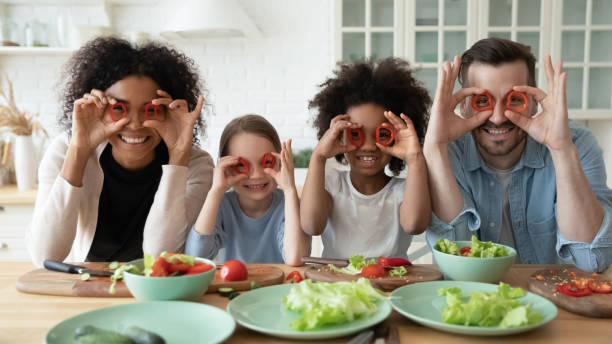Image of family at kitchen table holding veggies around their eyes like glasses